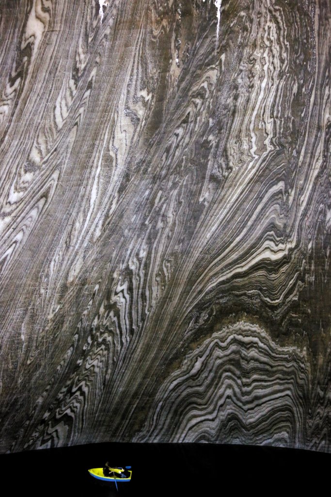 The patterns of the smooth, polished, salt-stone walls which line the 90-metre (295 ft) deep, bell-shaped, chamber of the Terezia Mine form a striking backdrop to the ink-black water of the underground lake.