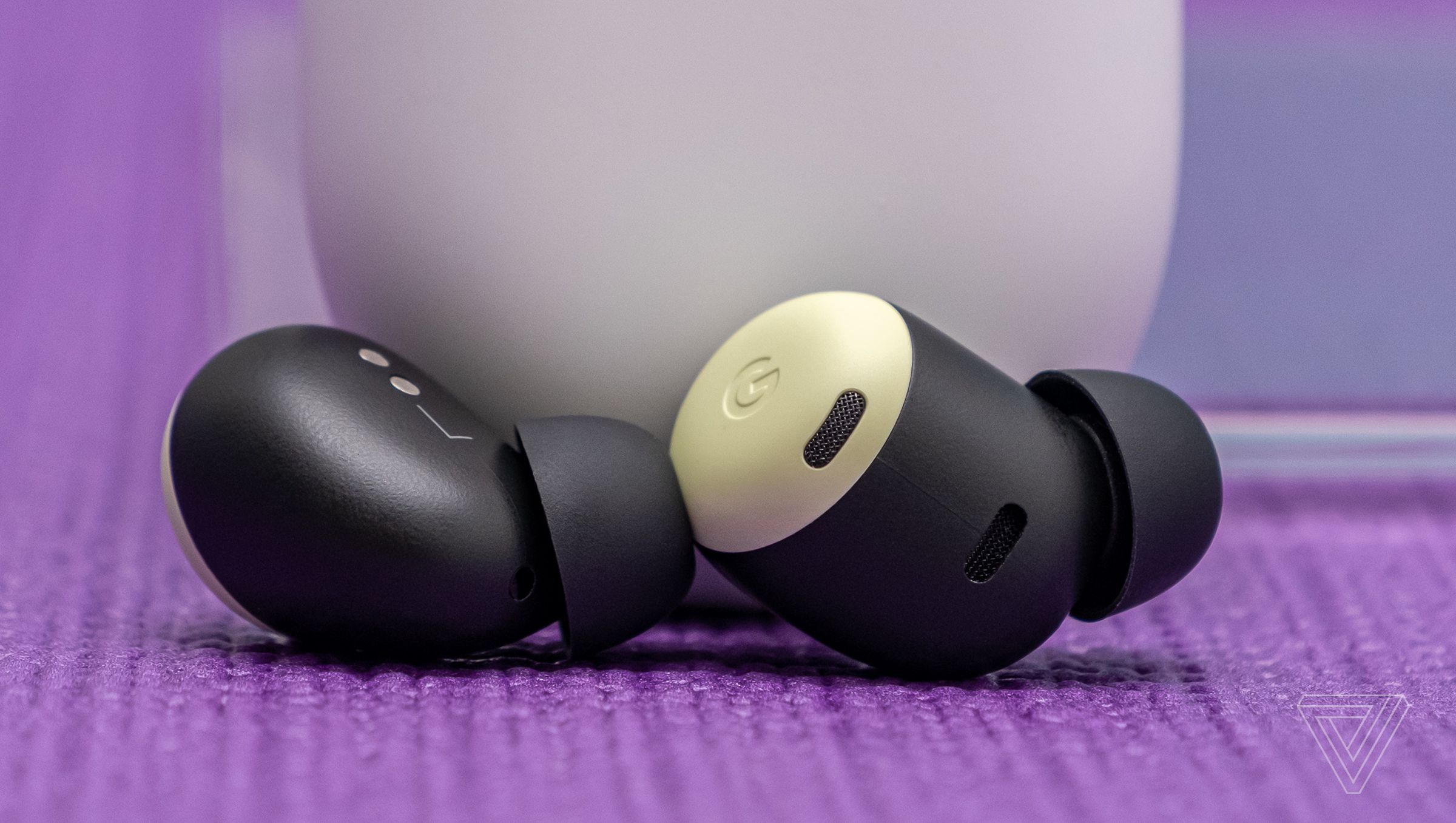 Google’s Pixel Buds Pro earbuds, in yellow lemongrass color, resting at the foot of their white charging case on a tabletop.