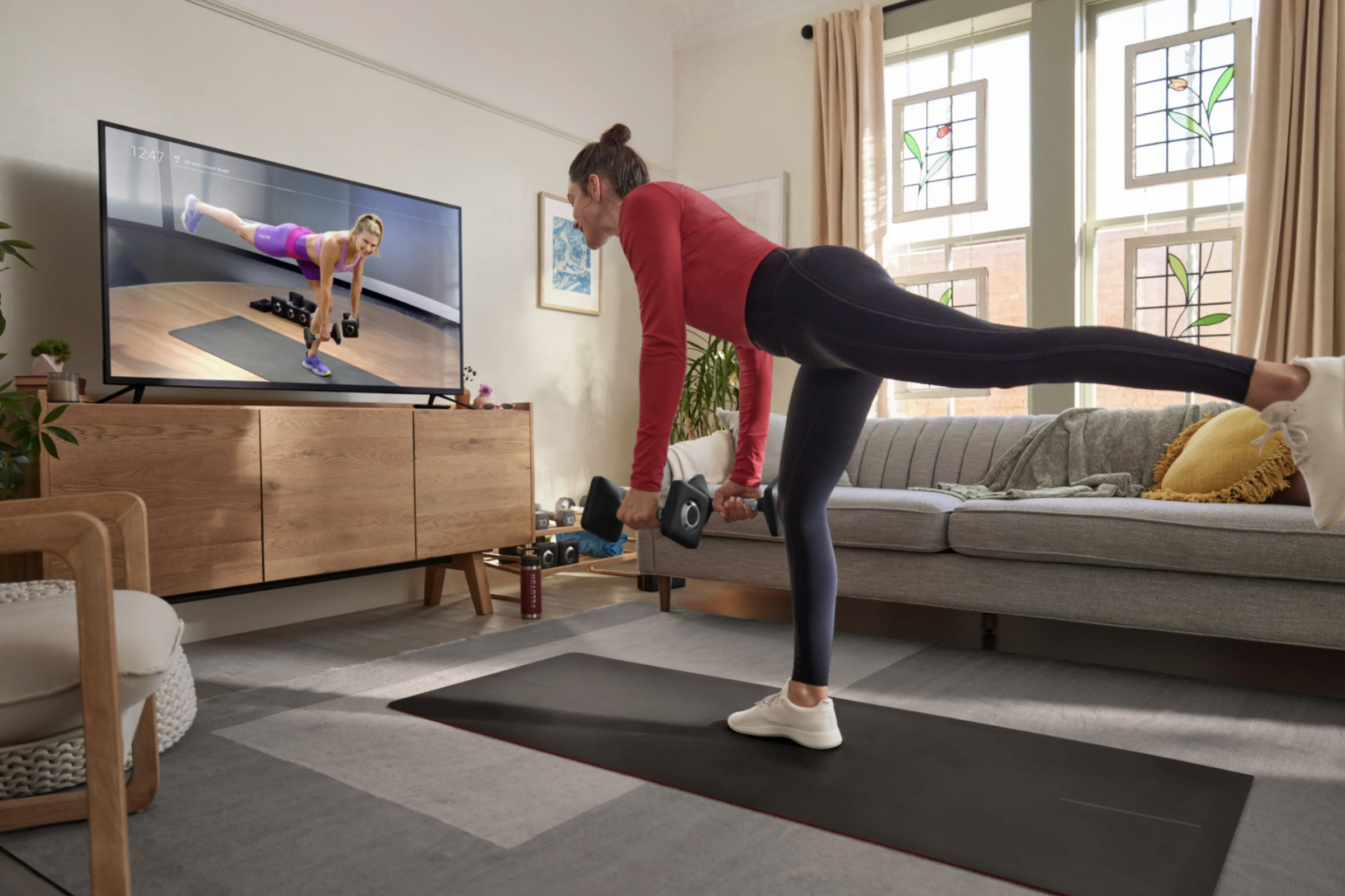 Person stretching in front of TV streaming Peloton subscription content.