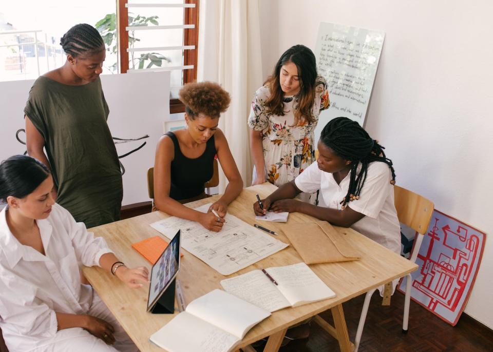 Here are 16 original tech startup ideas and how to create more. Pictured: five woman around a table working.