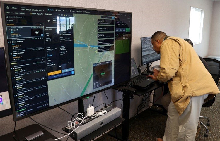 Man looking at a computer screen. On the left, there is a large monitor detailing a map and technological information.