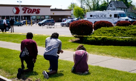 Three people paying tribute by kneeling on the grass opposite the car park of the Tops supermarket where people were killed