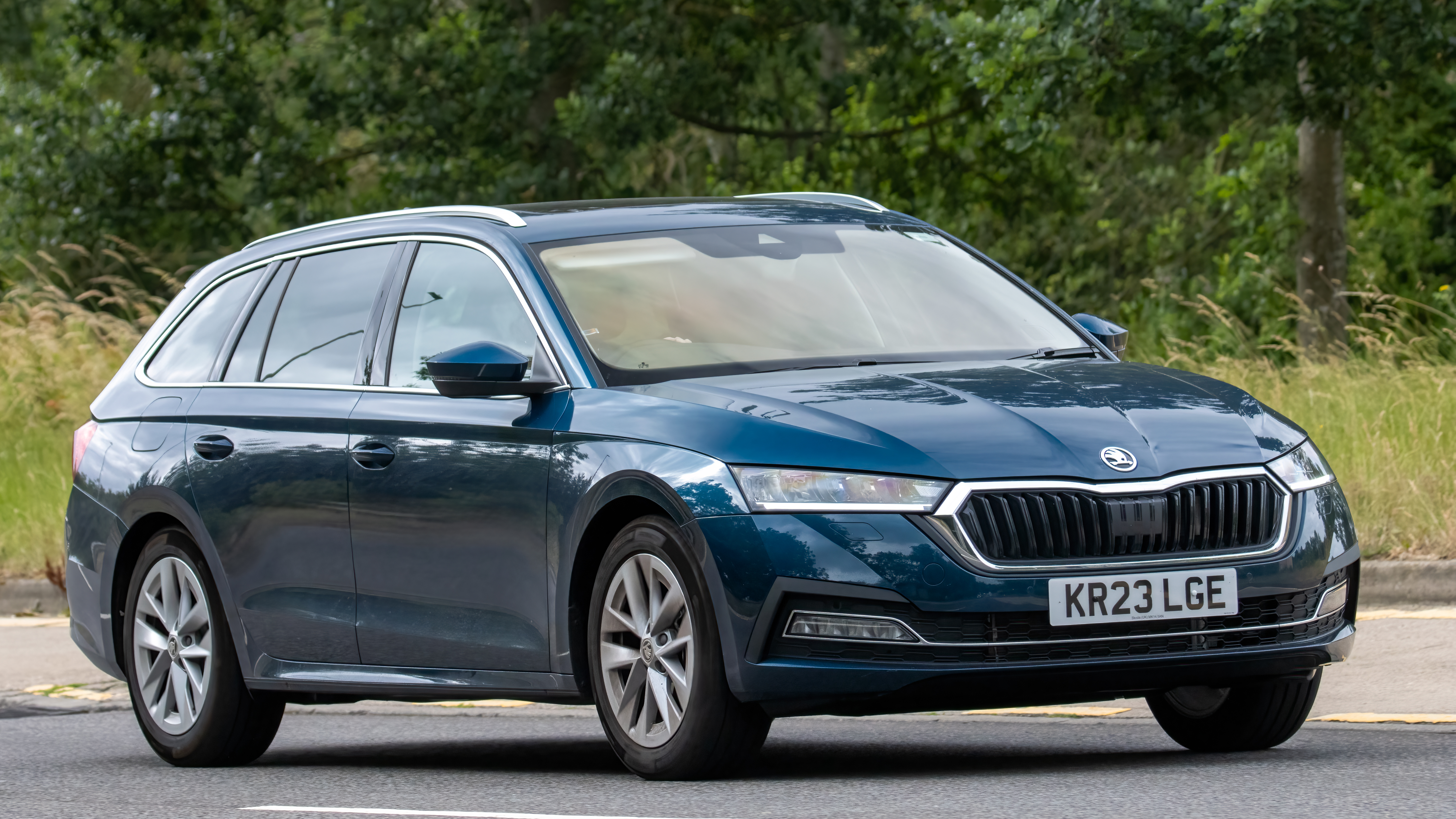 A 2023 blue Skoda Octavia hybrid electric estate car drives on an English country road