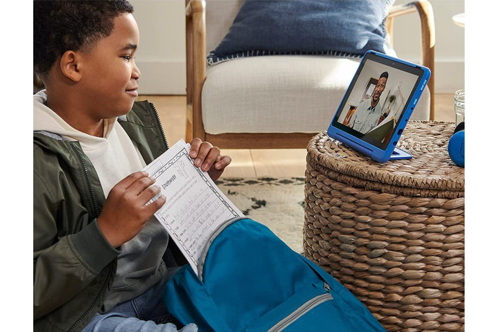 A boy with a worksheet watching video on a blue Amazon Fire HD 10 Kids Pro.