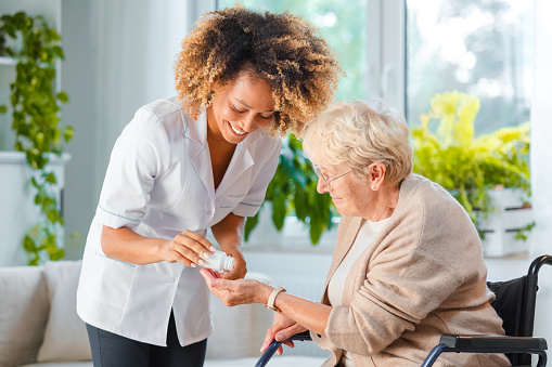 Home nurse giving pills an elderly lady