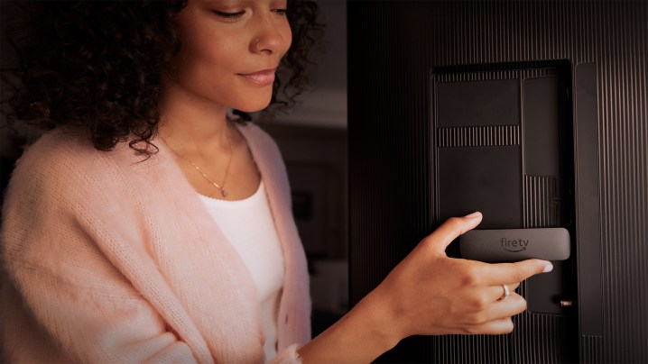 A woman plugs an Amazon Fire Stick into a TV.