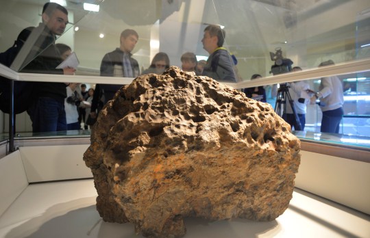 Reporters gather around a piece of a meteorite lifted from the bottom of the Chebarkul Lake and placed on display in a museum in Chelyabinsk