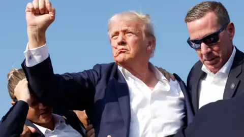 Getty Images Donald Trump with blood on his face holding up his fist to crowd after an assassination attempt