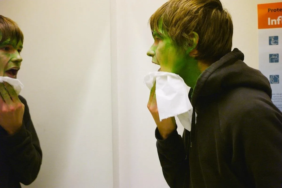 Teen applying green face paint in a mirror.