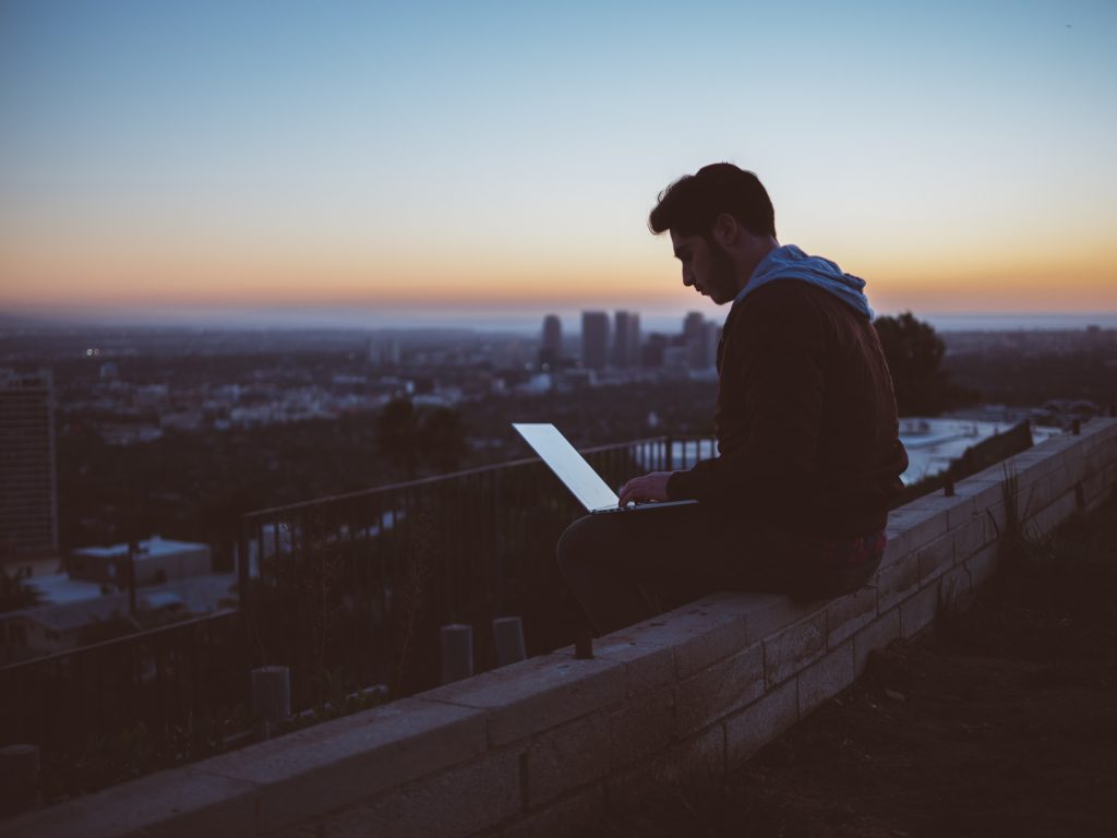 Mann mit Laptop sitzt auf Mauer und genießt seine Unabhängigkeit.