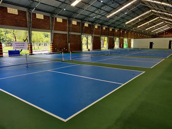 Four empty blue pickleball courts at Benjakitti Forest Park with green spaces in between.