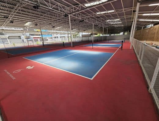 Indoor pickleball court at Club 46 in Bangkok, featuring blue court and red surroundings under a covered structure.