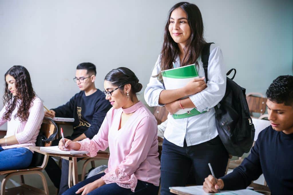 A female student standing and smiling among other students in the classroom.