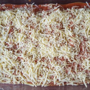 Die gefüllten mit Tomatensoße übergossenen Cannelloni mit geriebenen veganem Käse bestreuen und ab in den Ofen