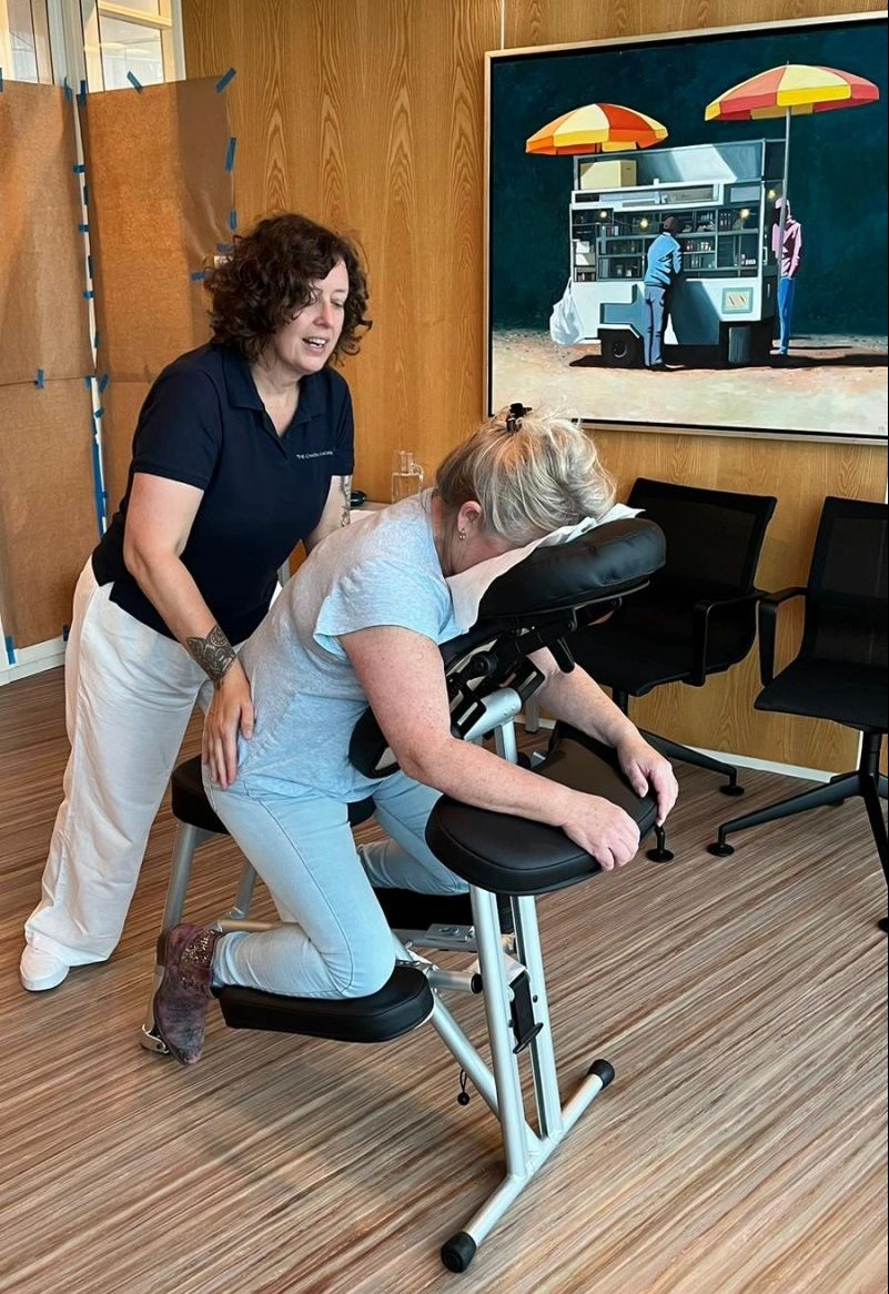 Ang`èle staat achter de massagestoelen en masseert de rug van een klant.