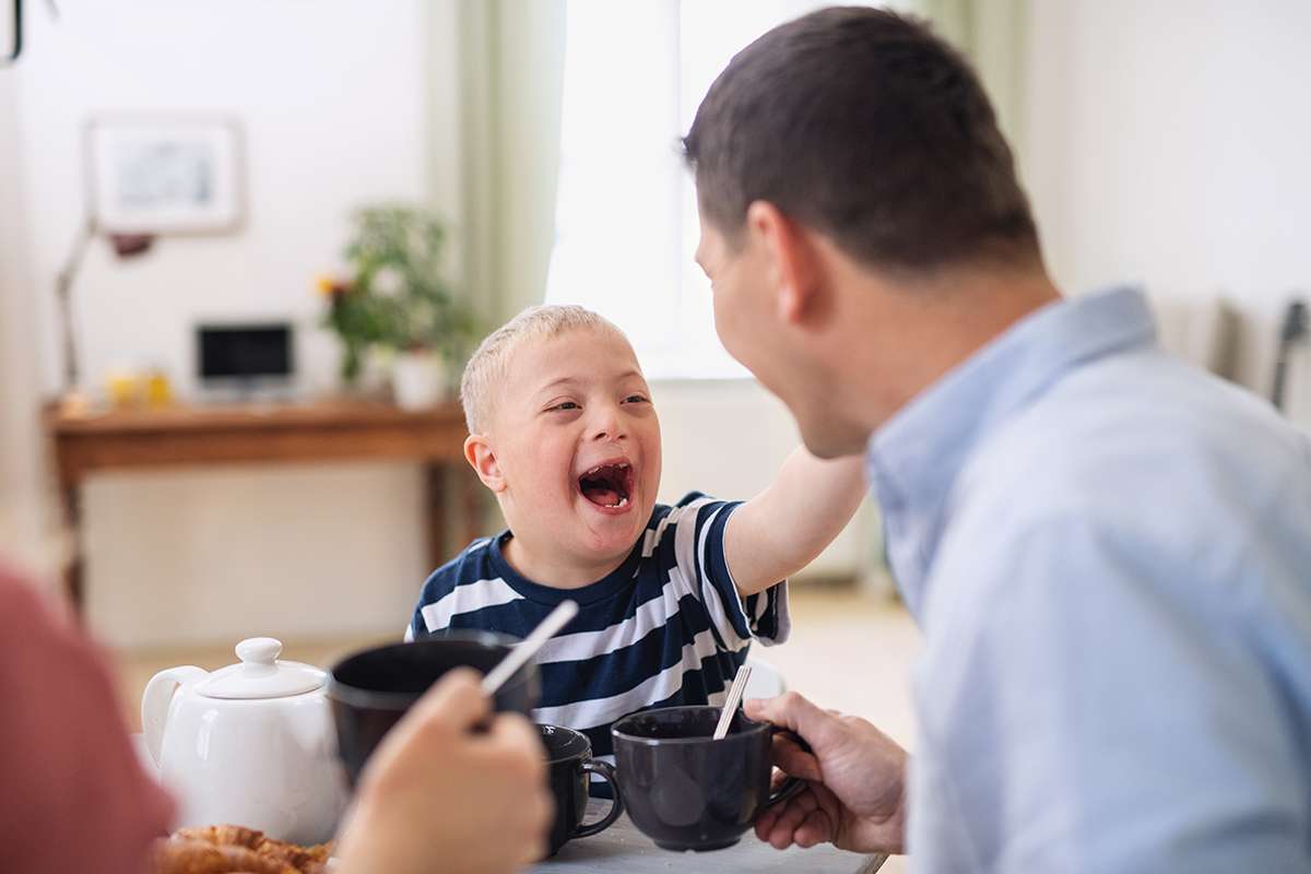 paediatrie happy family with down syndrome son table laughing when having breakfast 1200 Praxis für Ergotherapie, Physiotherapie und Wellnestherapie