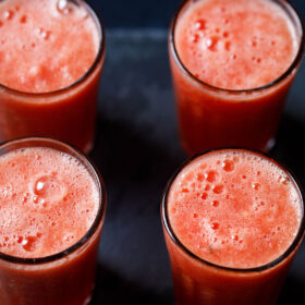 four tall clear glasses filled with watermelon juice on a black background
