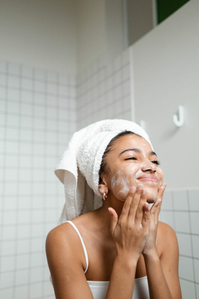 Woman applying skin care cream to her face with a towel in her hair