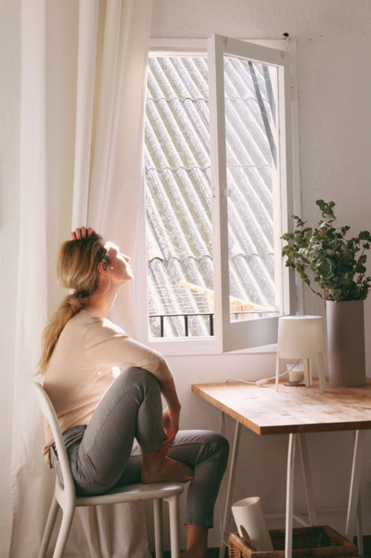 A woman sitting at her computer, looking uninterested, and gazing out of the window with a bored expression.