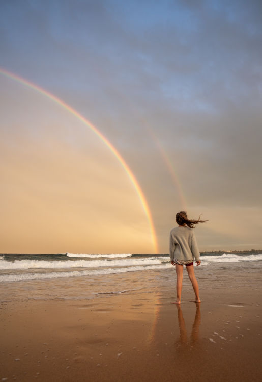 Woman healing by walking on the beach with a rainbow