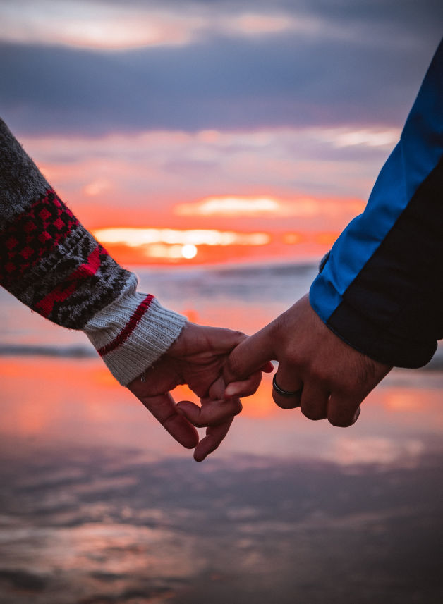 Holding hands over the sea with a sunset in dark blue, pink and red colors