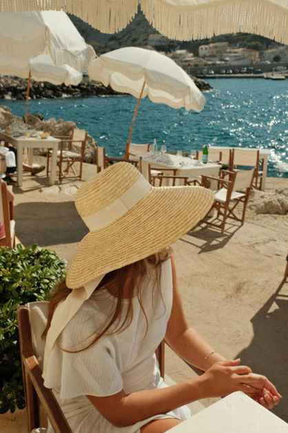 Woman wearing a timeless fashion trend hat and recycled fashion dress sitting on a cliff restaurant 