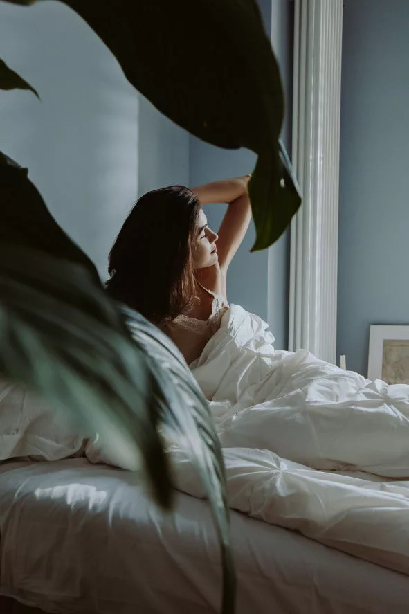 A woman waking up early in her bedroom with green leaves in front of her