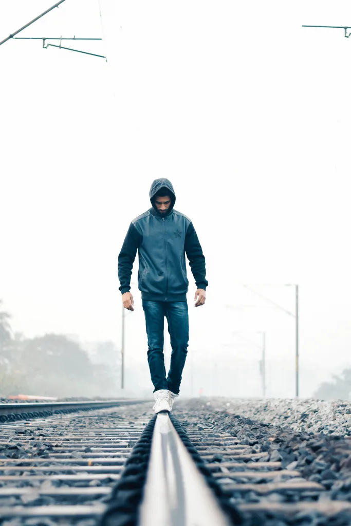 man walking on a trailroad in rain with a jacket