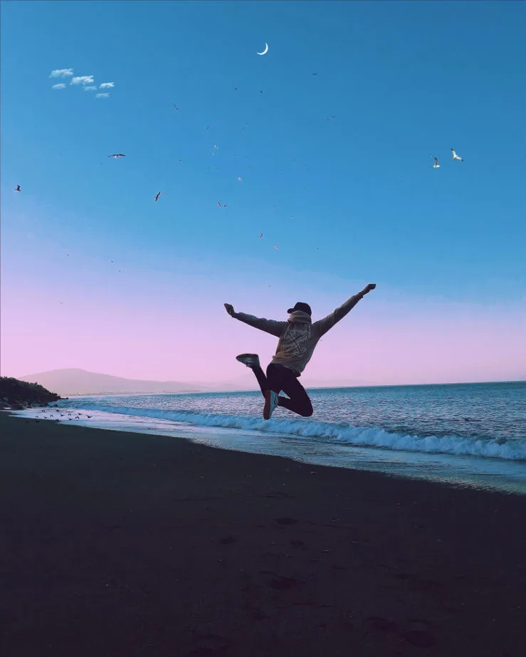 Man jumping in front a the dark ocean with purple and blue skies