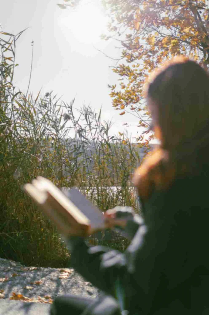 Silhouetted woman reading a book outside. Pexel free to use image.