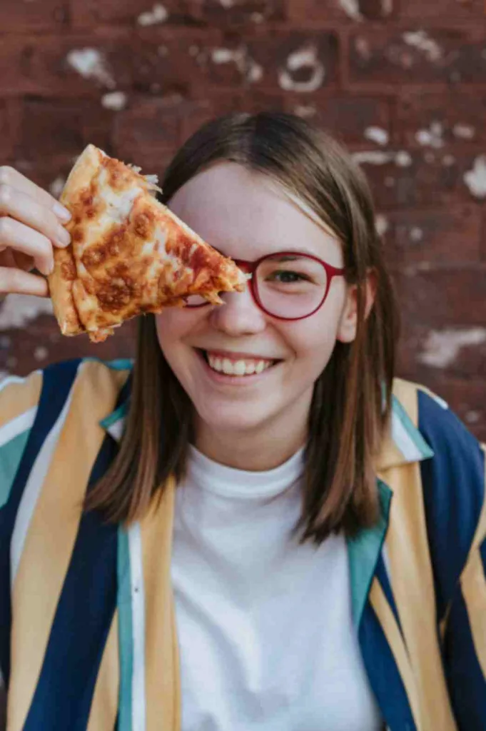 Teen girl smiling while with a slice of pizza showcasing best books 2024 for Young Adults.
