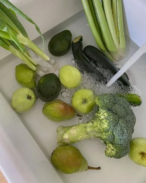 Green vegetables being washed in a white sink