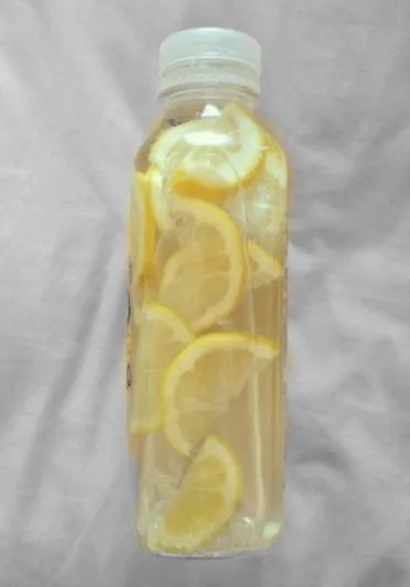 Lemon water in a glass bottle laying on white sheets