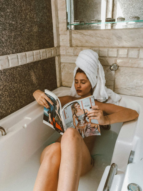 woman in the bathtub reading a magazine while doing a face mask
