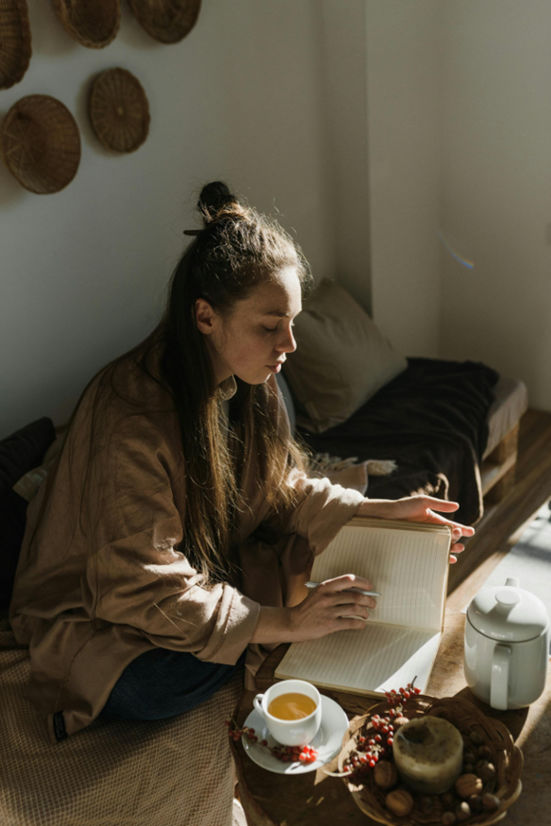 Una mujer está sentada en un sofá y escribiendo un diario.
