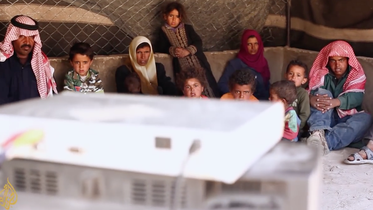 After starting the generator and setting up their TV and receiver, a Bedouin family in Petra watches television together. Screenshot from a video by Al-Jazeera: “The Bedouin of Petra”.
