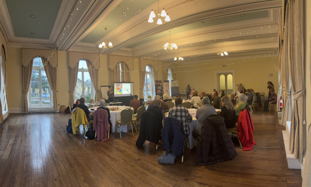 Image of event, multiple people sat around tables looking towards a presentation.
