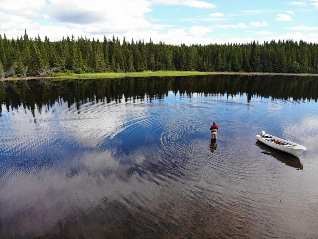 Fly Fisherman wading by his boat - fishing for trout and Arctic char at Skålestrømmen, Norway
