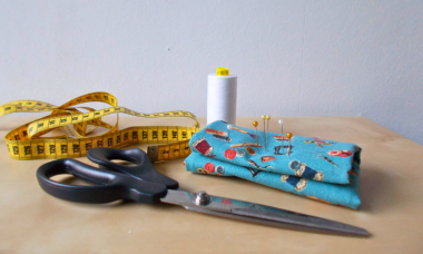 Een schaar, een gele lintmeter, wit naaigaren en een speldenkussentje.