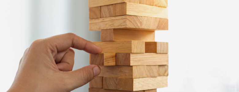 Een hand neemt een houten blokje van Jenga uit de toren.