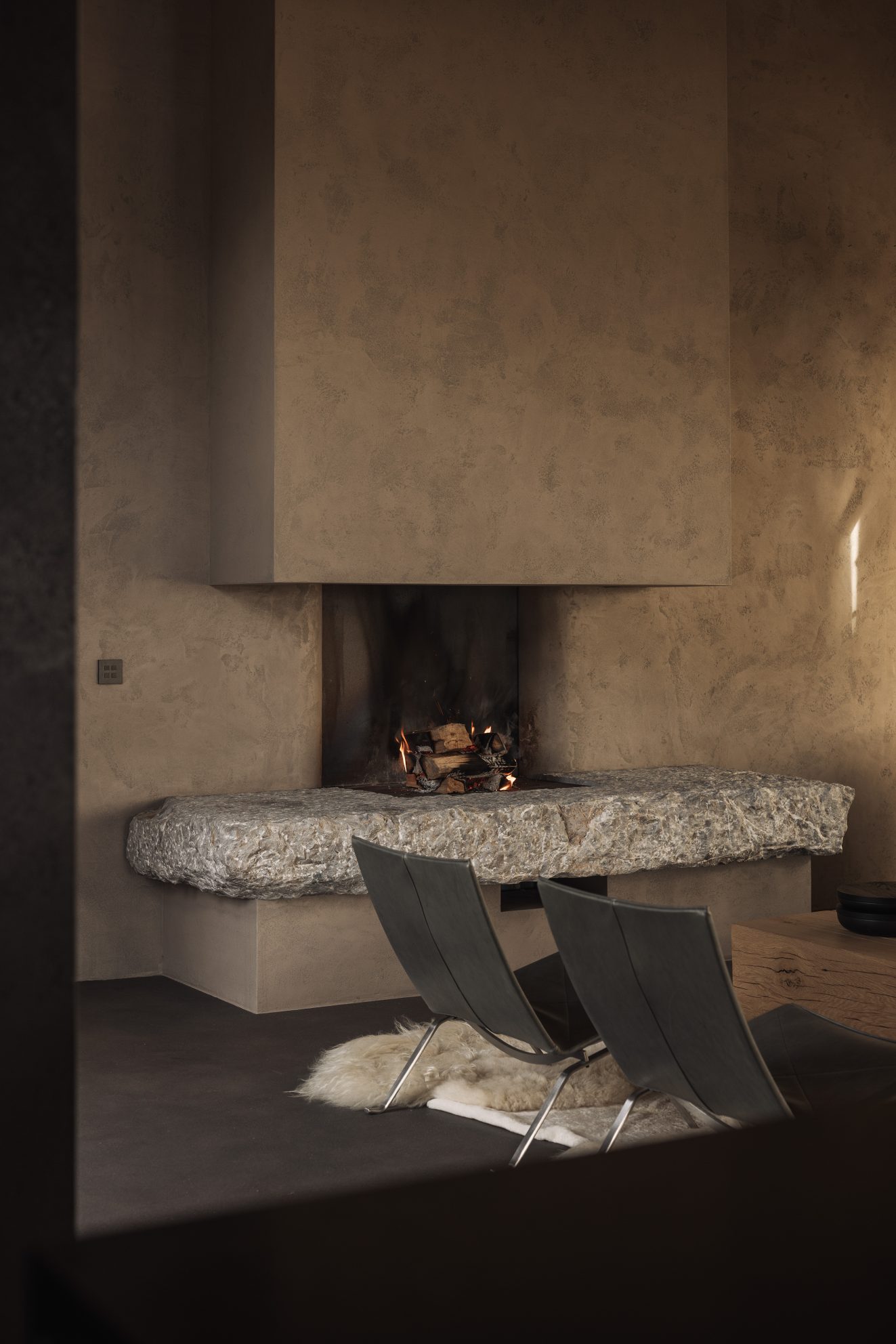 Open haard met ruwe stenen haardbank en twee lage stoelen op een vacht