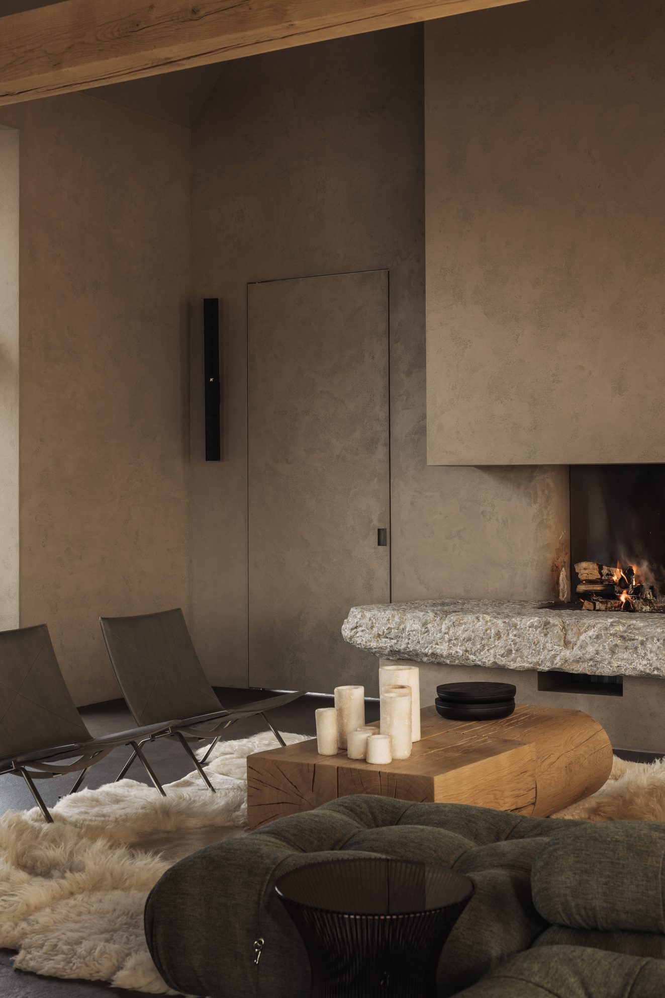 Leefruimte met open haard, lage stoelen en houten salontafel op schapenvacht