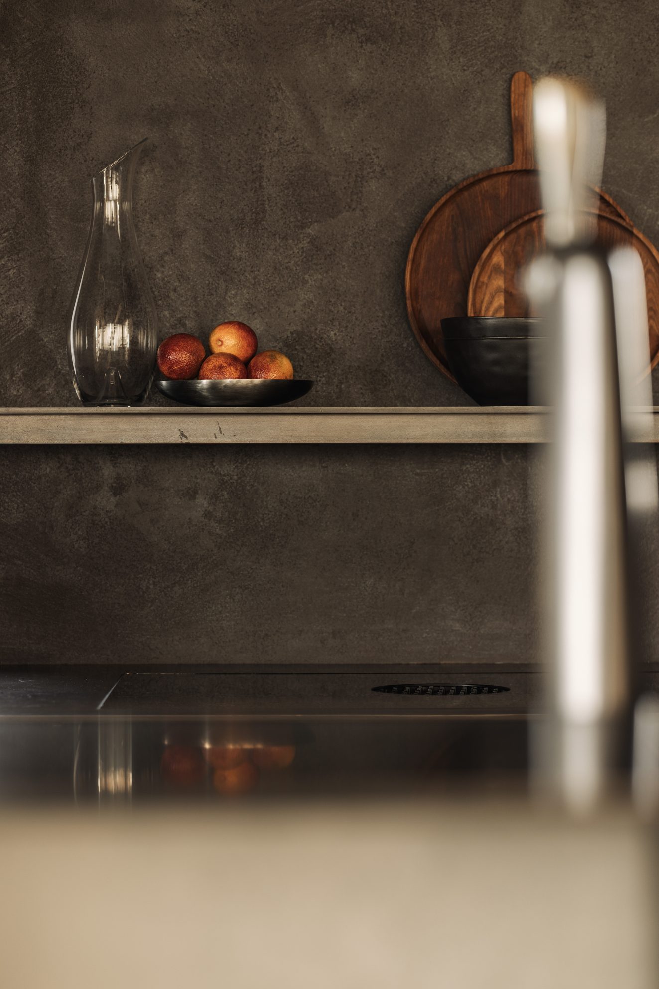 Fruitschaal en karaf op een smalle keukenplank tegen donkere wand