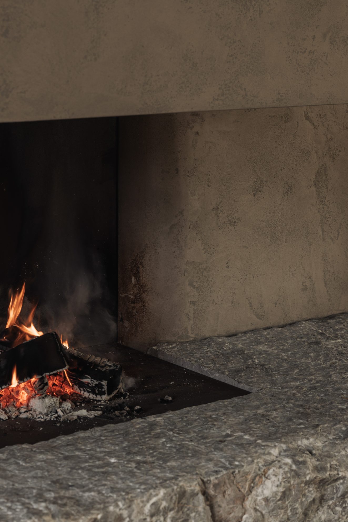 Close-up van brandend vuur naast een ruwe stenen haardplaat