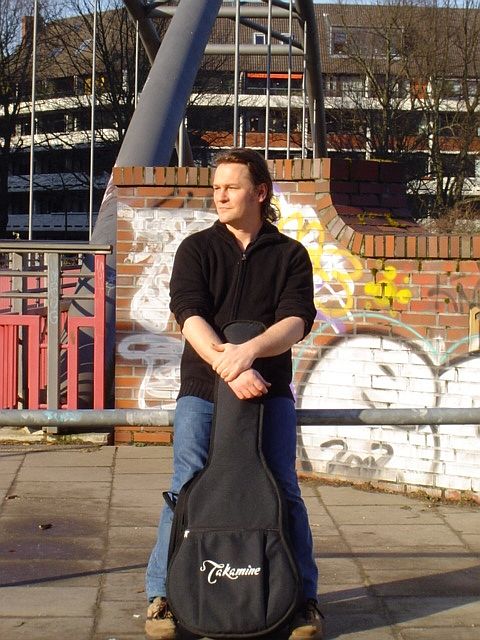 Singer Songwriter Torsten Q mit Gitarre vor einer Brücke in Hamburg Winterhude. 