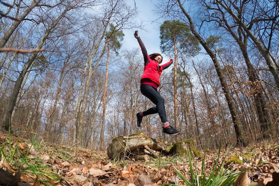 active senior woman running in the forest on a warm day in early spring