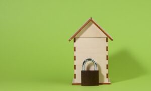 Miniature wooden house and metal lock on a green background, security concept