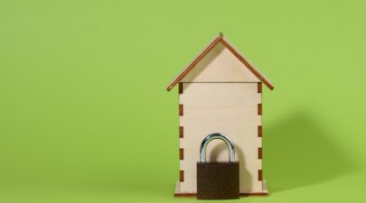 Miniature wooden house and metal lock on a green background, security concept