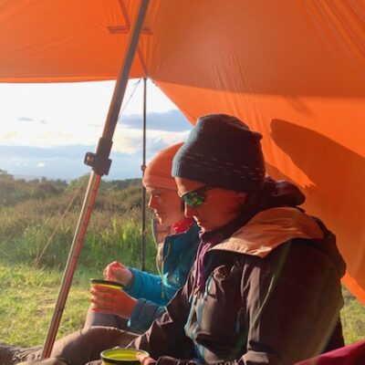 Women sit in the evening sun under a tarp in the Cairngorms