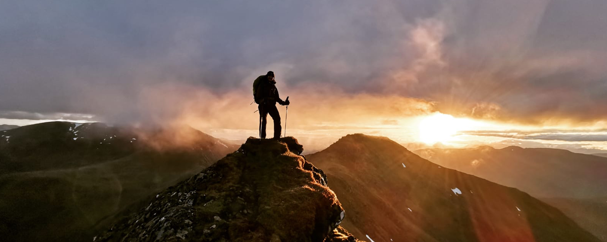 Woman stands on mountain-top at sunset in the Mullardoch mountains, Scotland